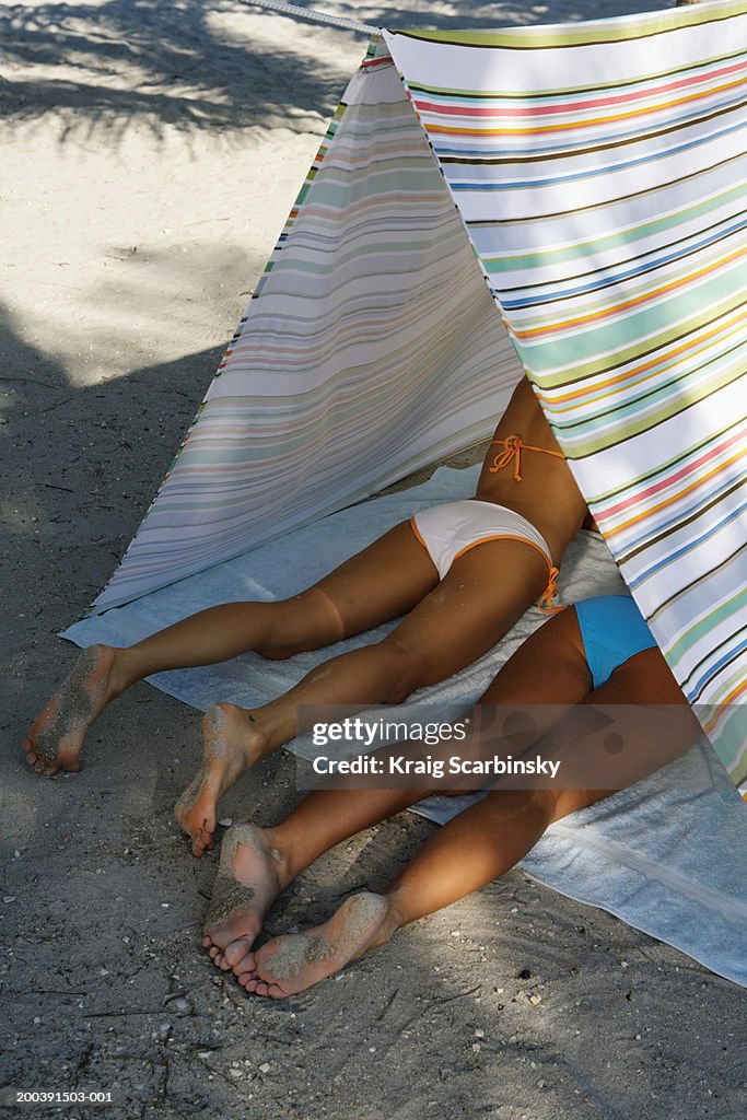 Two young women lying in tent on beach, elevated view, rear view