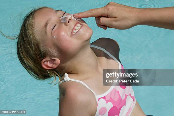 girl (7-9) by swimming pool, having sun cream being applied on, - sun on face stock-fotos und bilder