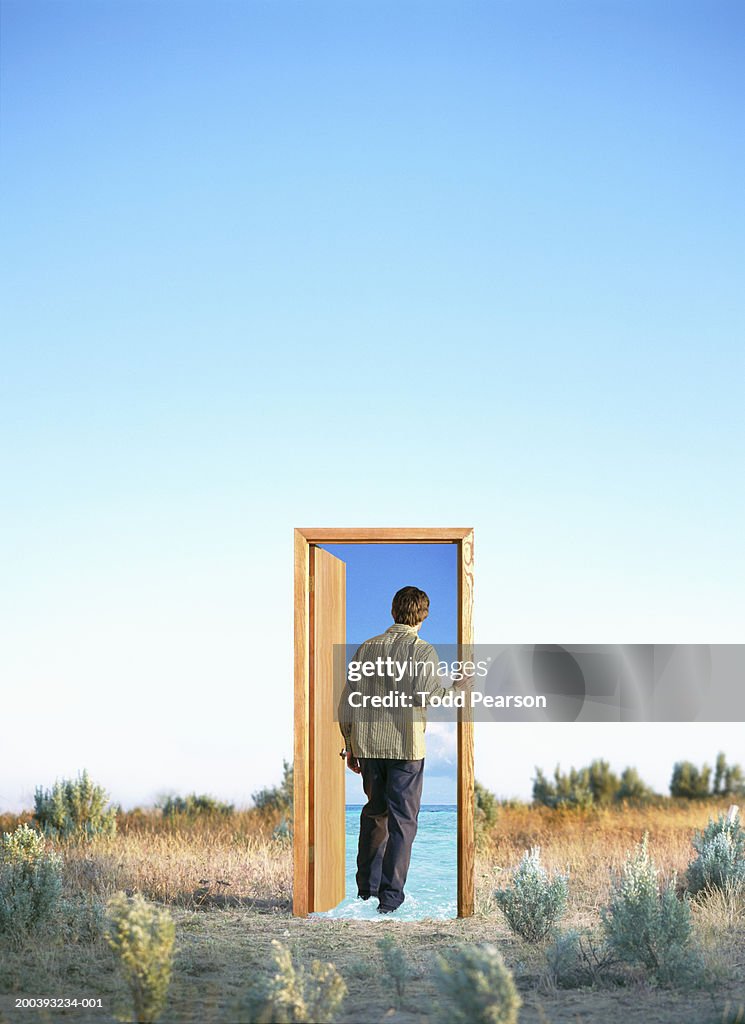 Man walking through doorway with ocean, in desert