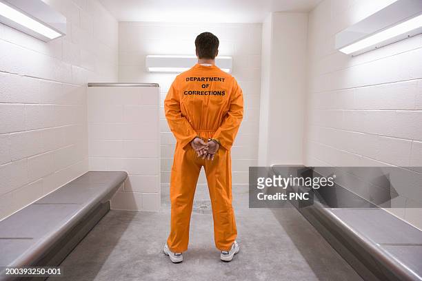 man wearing prisoner uniform, standing in holding cell, rear view - prison jumpsuit stock pictures, royalty-free photos & images
