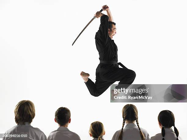 kempo karate instructor jumping in air with sword in front of students - boy barefoot rear view stockfoto's en -beelden