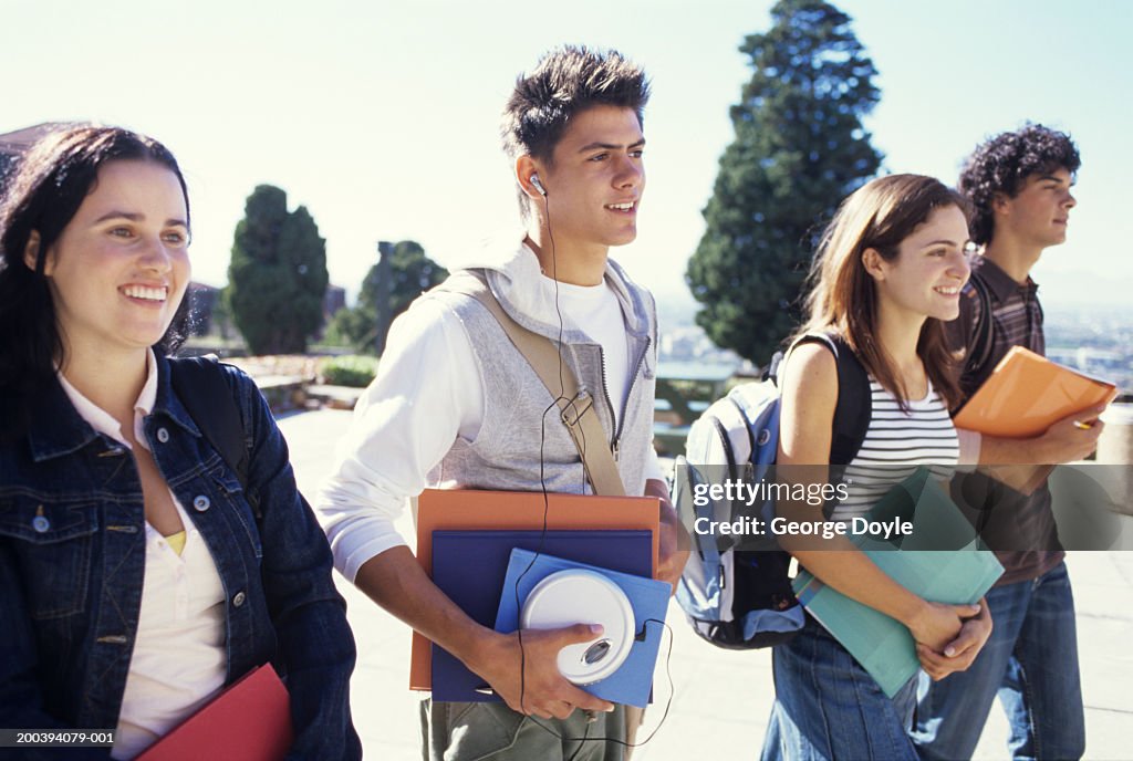 Young women and men walking carrying folders, smiling
