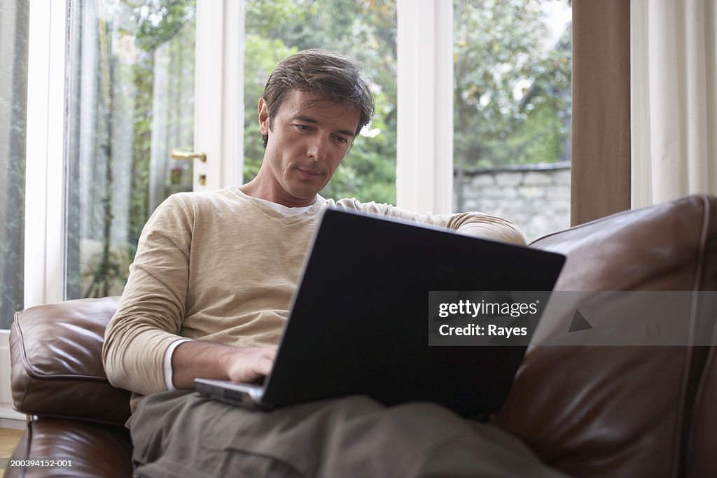 Mature man sitting on sofa using laptop