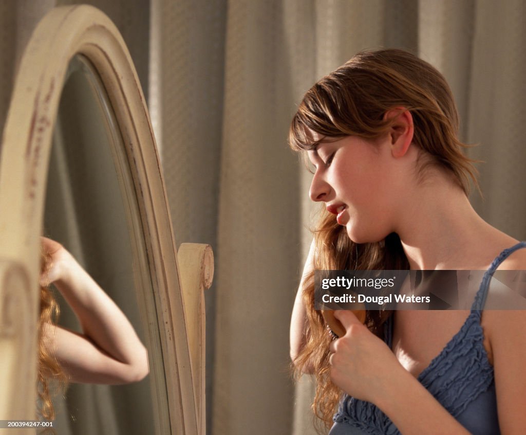 Young woman brushing hair in front of mirror