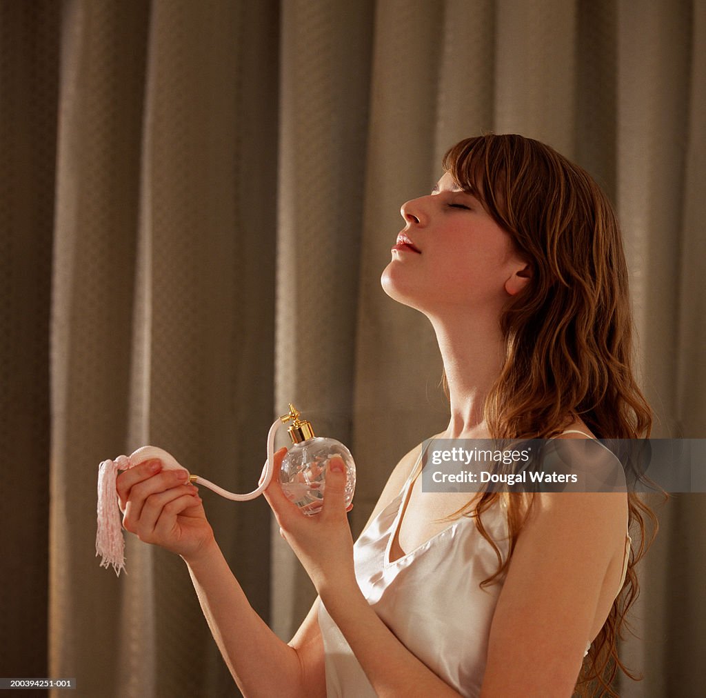 Young woman spraying perfume on neck, eyes closed