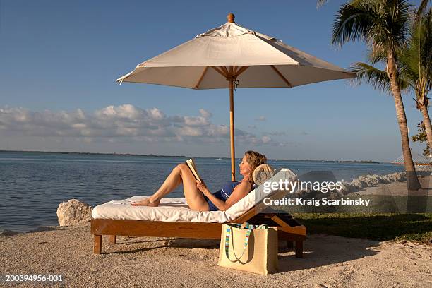 mature woman reclining on sun lounger holding book, eyes closed - reclining chair stock pictures, royalty-free photos & images