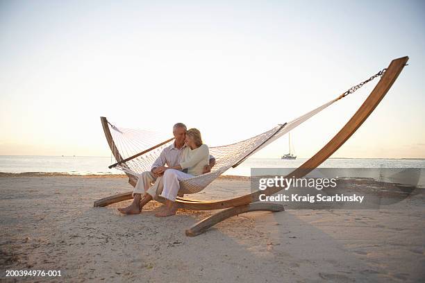 mature couple sitting on hammock on beach, heads together - florida beach stockfoto's en -beelden