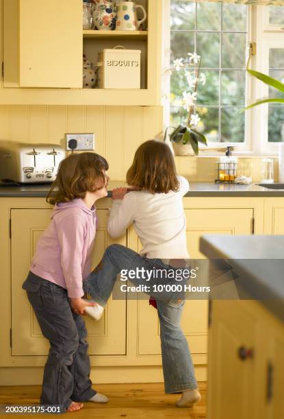 twin sisters (5-7) reaching for biscuit tin in kitchen - child cookie jar stock pictures, royalty-free photos & images