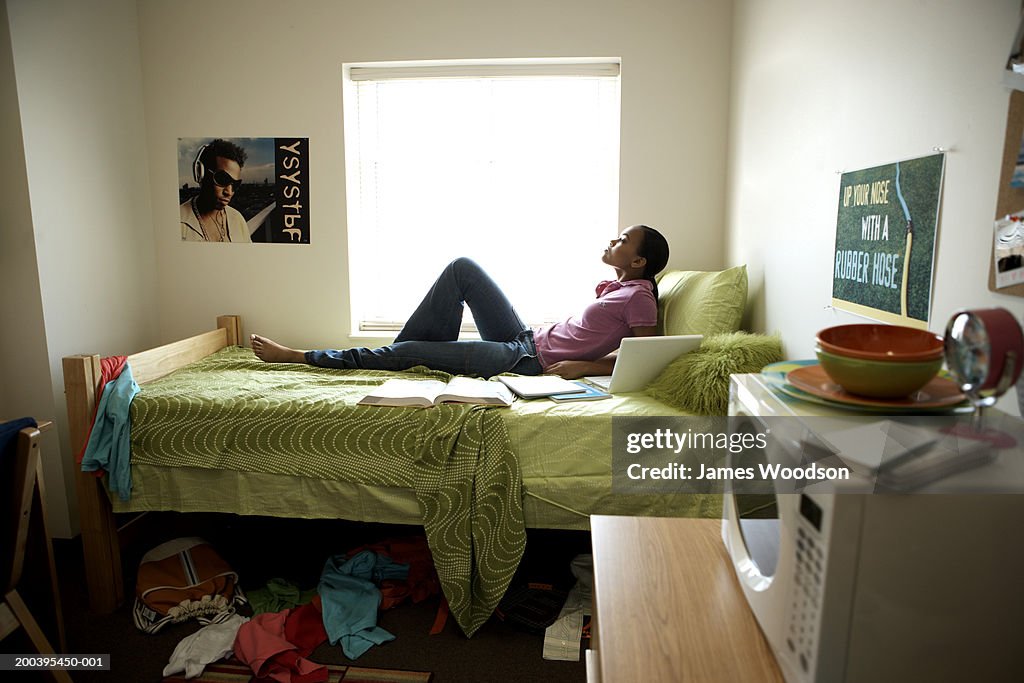 Young woman lying on bed in dorm room, side view