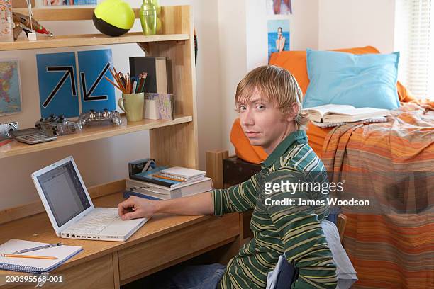 young man smiling at desk in dorm room, portrait - university student portrait stockfoto's en -beelden