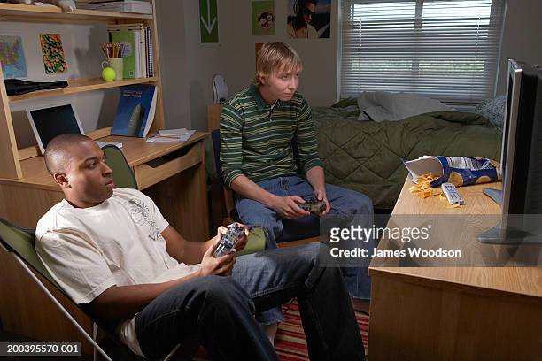 two young men playing video game in dorm room - rivaliteit stockfoto's en -beelden