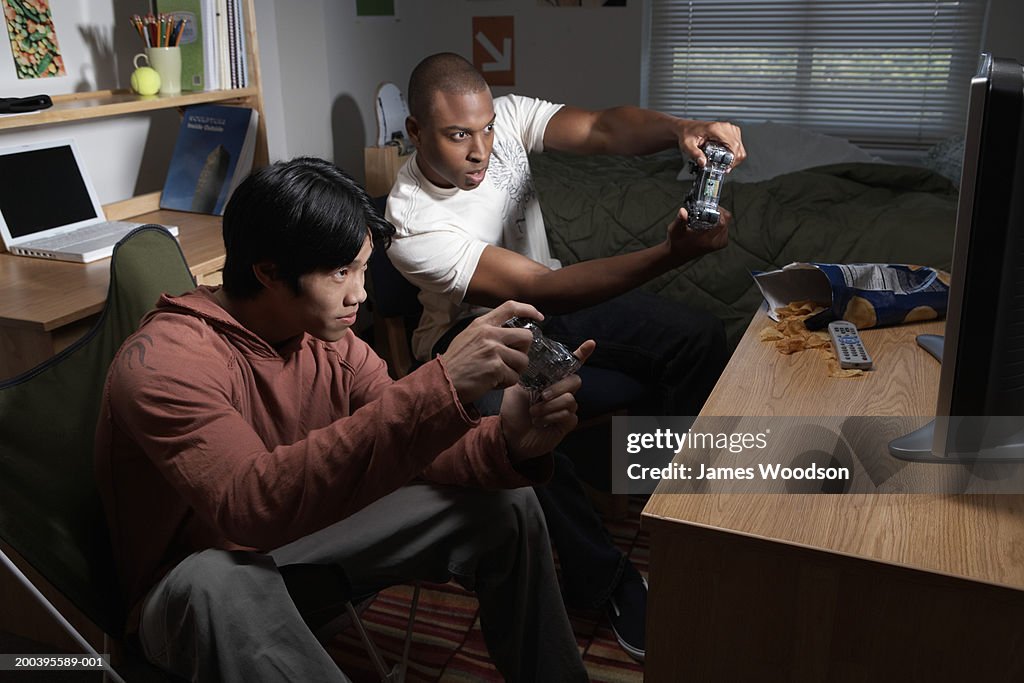 Two young men playing video game in dorm room, side view