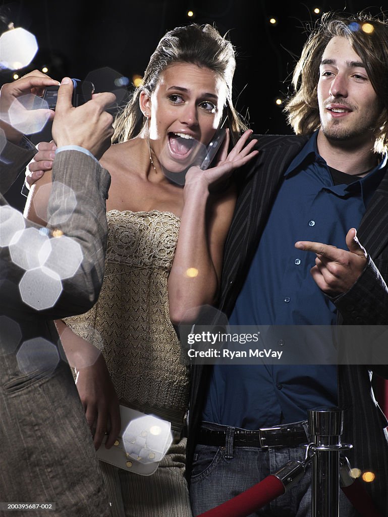 Young man taking photograph of young man and woman behind rope