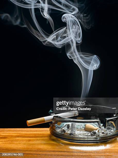 burning cigarette in ashtray on table - cigarettes stock-fotos und bilder