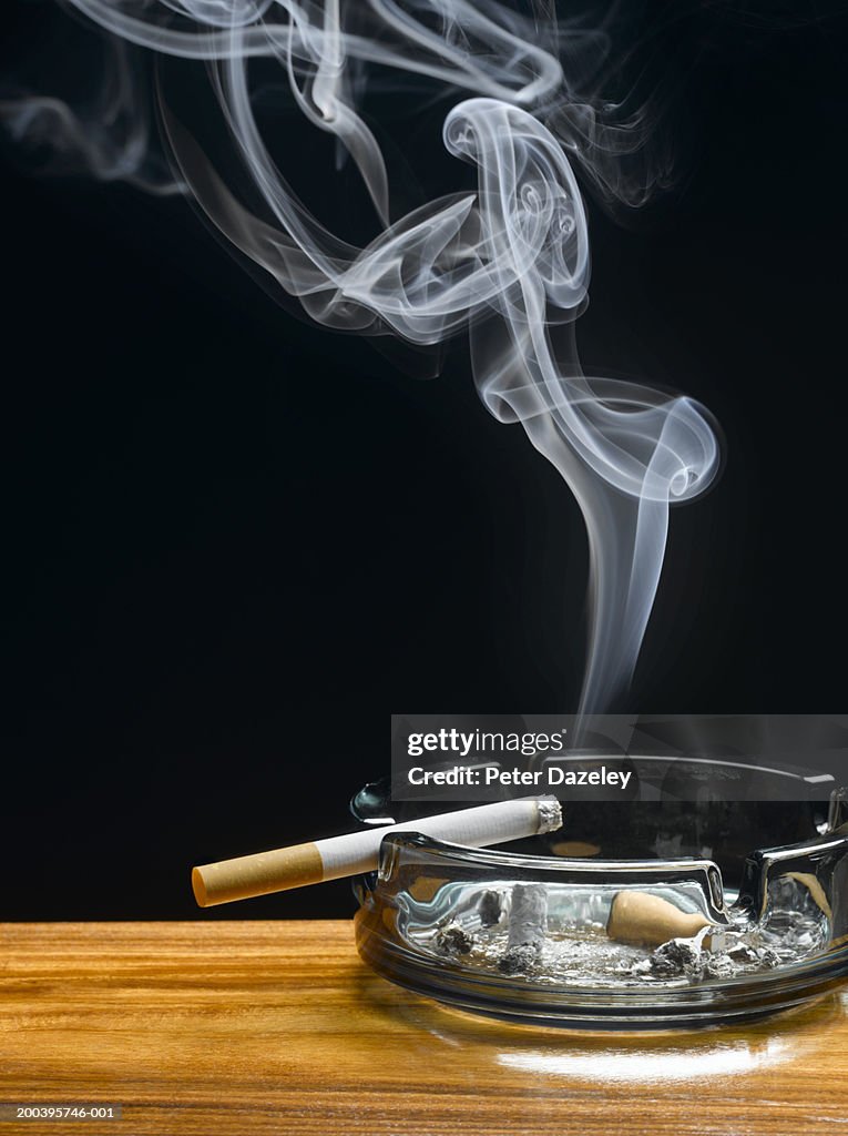 Burning cigarette in ashtray on table