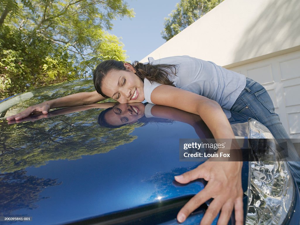 Young woman hugging car, smiling, eyes closed