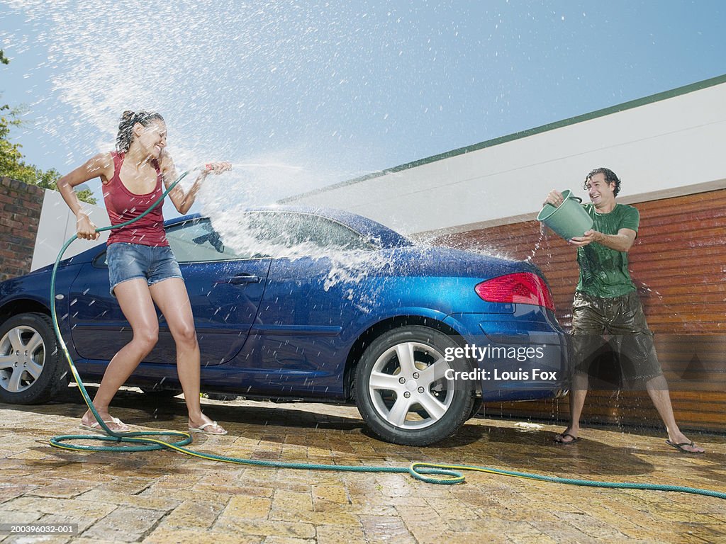 Young couple having water fight by car