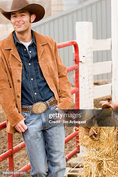 cowboy leaning against fence, smiling, portrait - leather belt stock-fotos und bilder