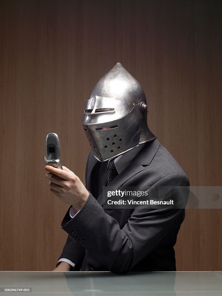 Businessman man wearing knight helmet, holding mobile phone