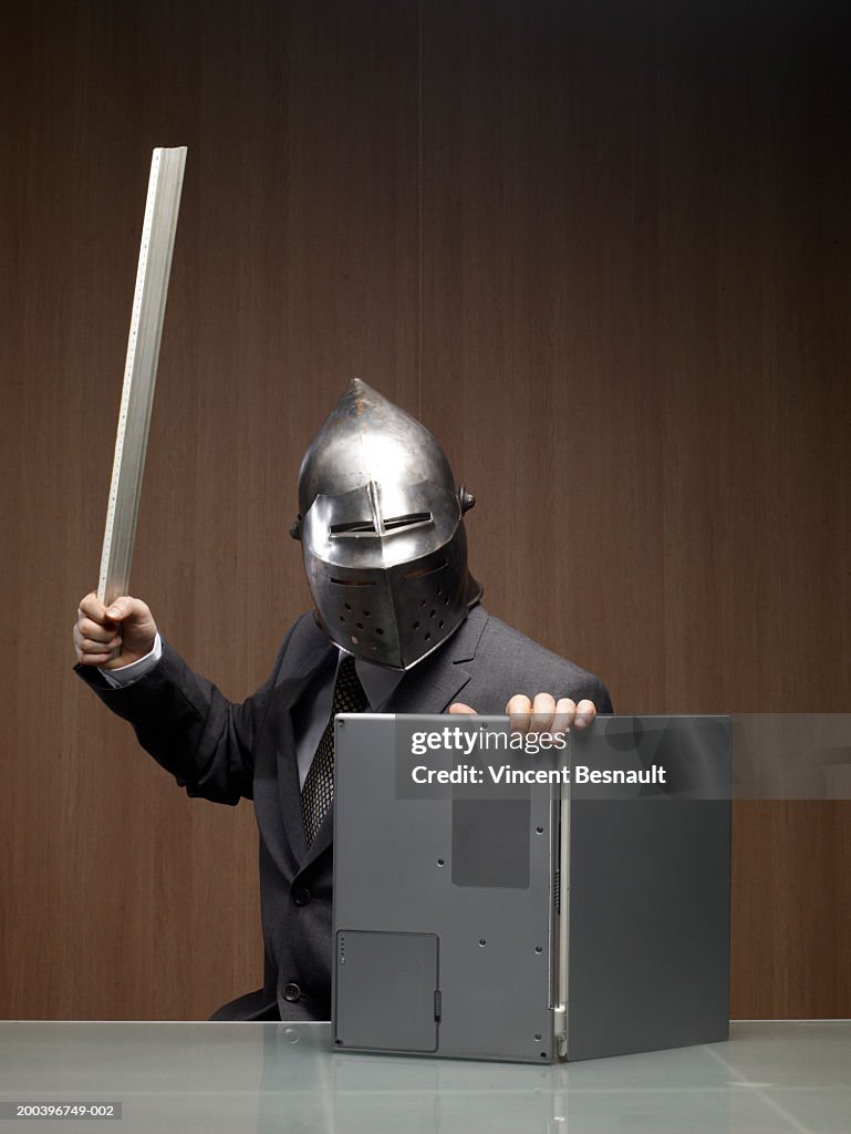 Businessman man wearing knight helmet, using laptop as shield