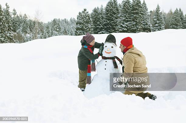 father and son (8-10) either side of snowman, side view - pupazzo di neve foto e immagini stock