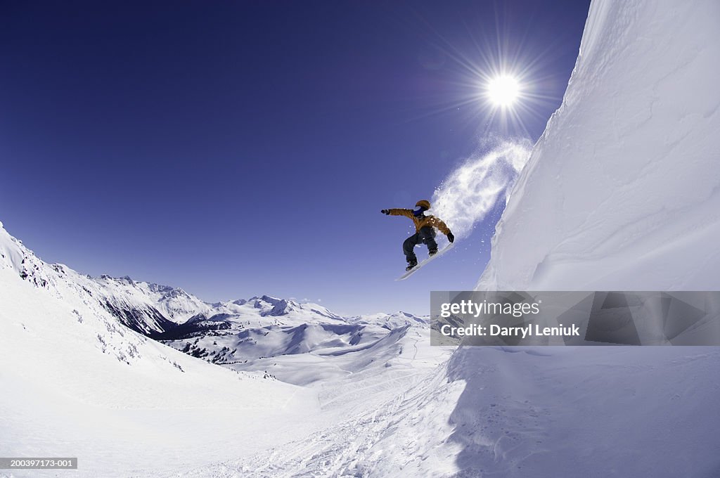 Male snowboarder jumping off cornice, low angle view