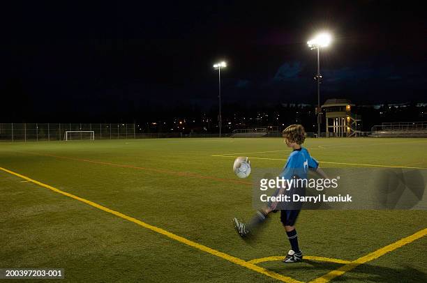 boy (10-12) kicking soccer ball on field, night (blurred motion) - flutlicht stock-fotos und bilder
