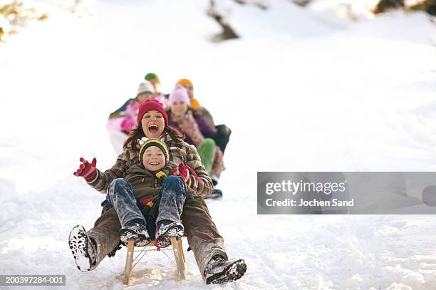 madre e hijo (8-10) deslizarse en trineo en la nieve, su familia en el fondo - sledge fotografías e imágenes de stock