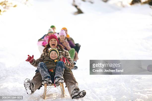 mother and son (8-10) tobogganing in snow, family in background - saturday stock pictures, royalty-free photos & images