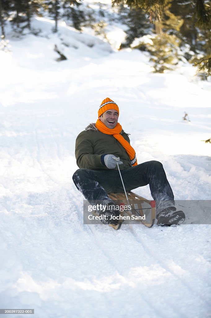 Mature man tobogganing on snow covered slope, smiling