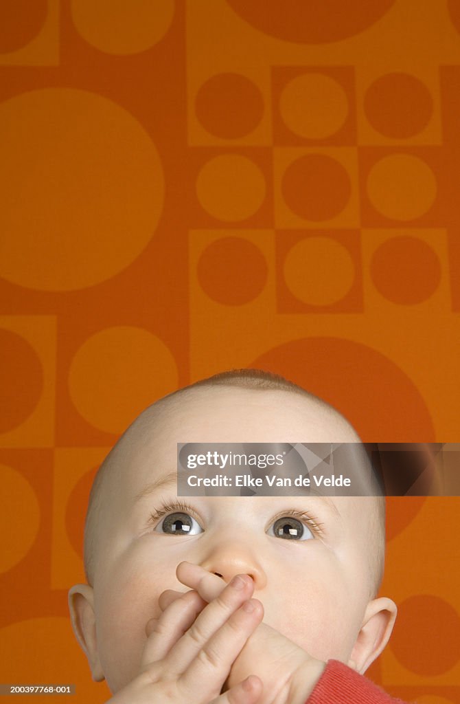 Baby boy (3-6 months) looking up, covering mouth with hands