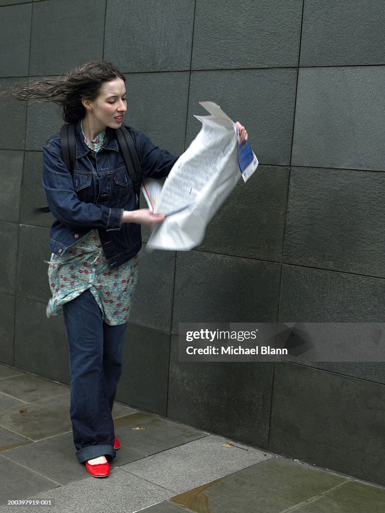 Young woman on street holding map blowing in wind