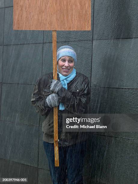 mature woman standing in rain holding placard, looking away - shivering stock pictures, royalty-free photos & images