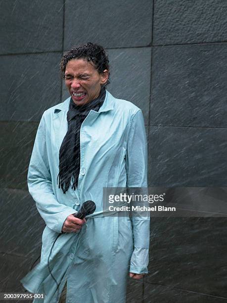 mature woman standing in rain holding microphone, eyes tightly closed - mike storen stockfoto's en -beelden