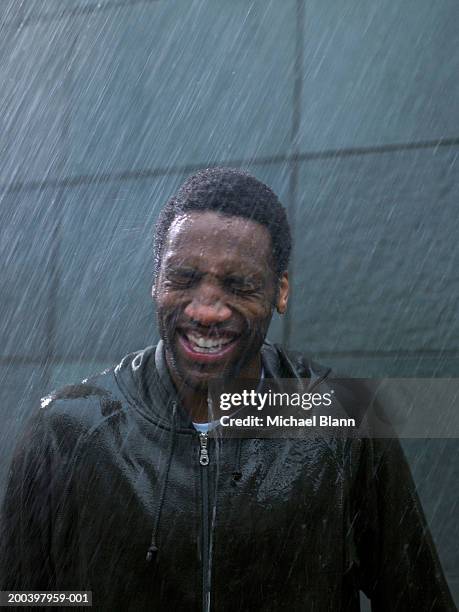 young man standing in rain, eyes tightly closed, close-up - sintflutartiger regen stock-fotos und bilder