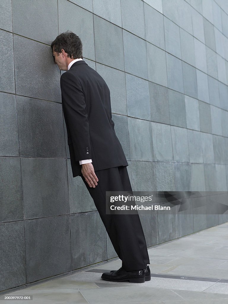 Businessman leaning forward, resting face against wall, side view