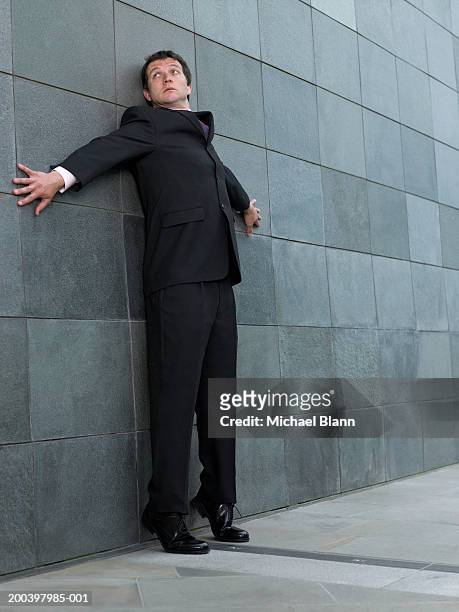 businessman on tip toes, back against wall, arms outstretched, looking up - paranoia stock-fotos und bilder