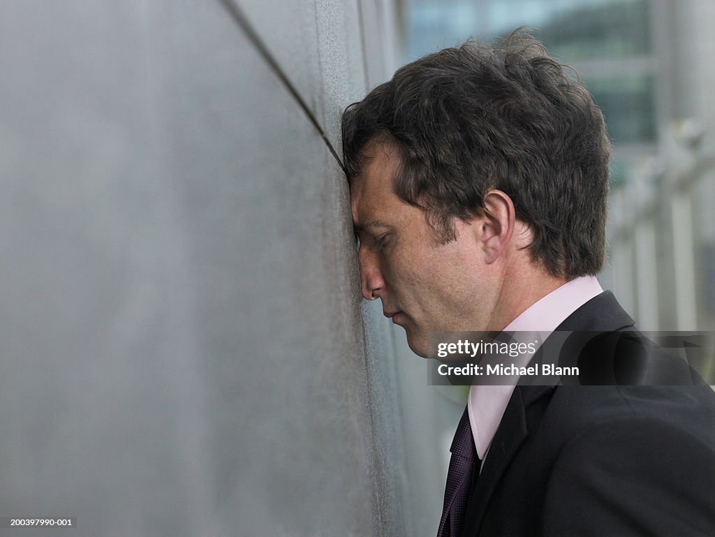 Businessman with face pressed against wall, profile, close-up