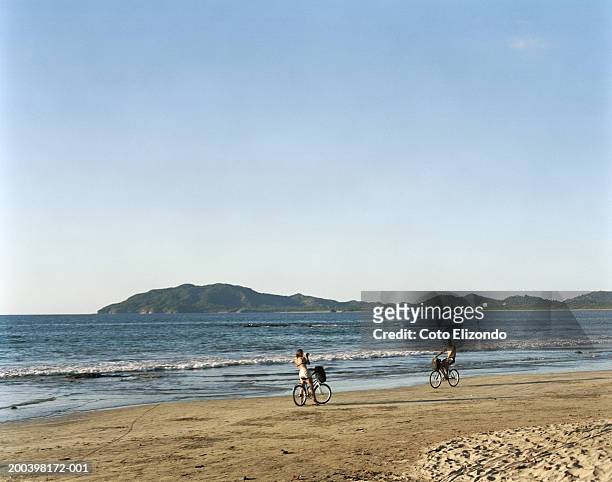 couple on bicycles at beach, woman taking photograph - playa tamarindo - fotografias e filmes do acervo