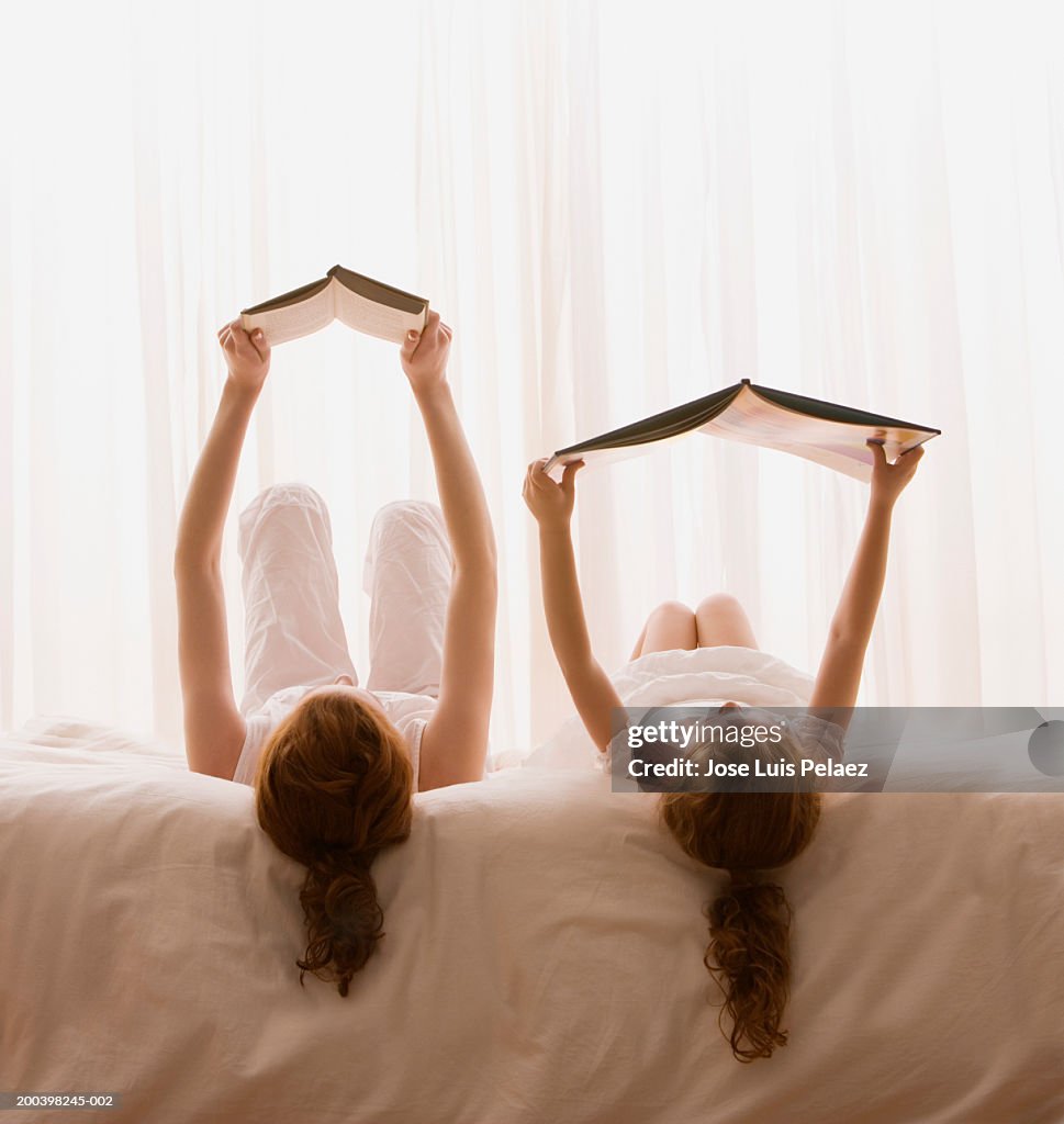 Mother and daughter (4-6) reading book in bed, rear view