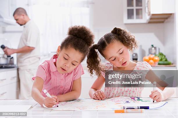 two sister (4-6) coloring on kitchen counter, dad in background - familia con dos hijos fotografías e imágenes de stock