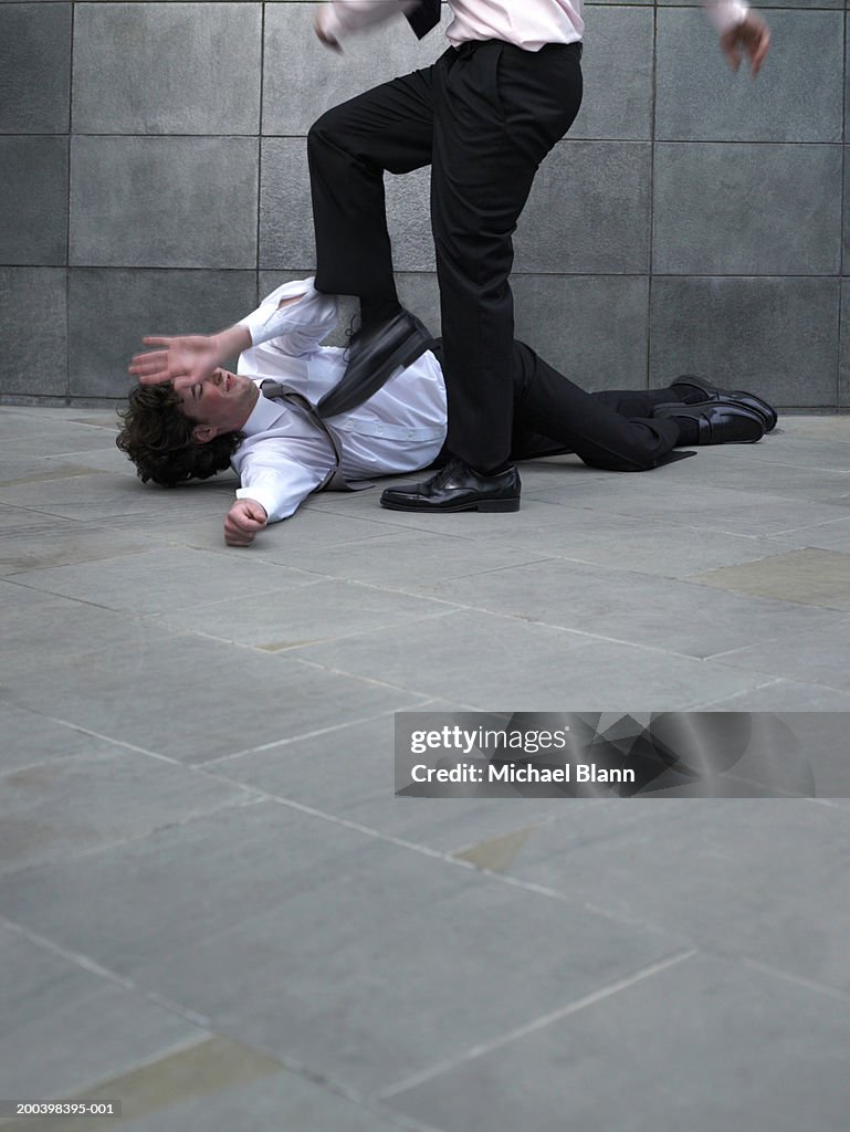Businessman kicking younger colleague lying on pavement (blurred motion)