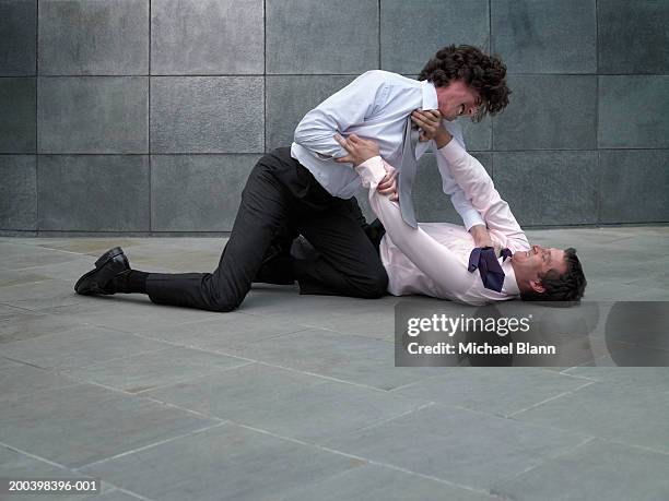 two businessmen fighting, younger man grabbing colleague's tie - mêlée stockfoto's en -beelden