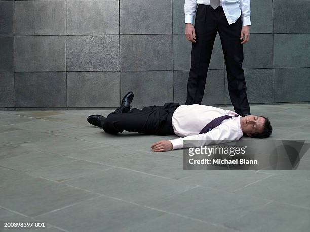 businessman standing over colleague lying on pavement - low section stockfoto's en -beelden