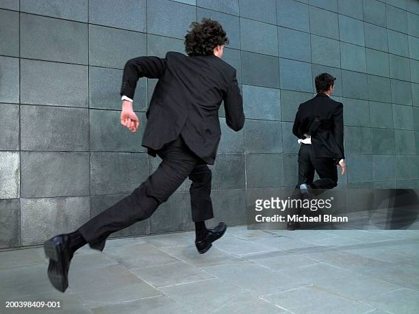 two businessmen running along street, rear view - chasing stockfoto's en -beelden