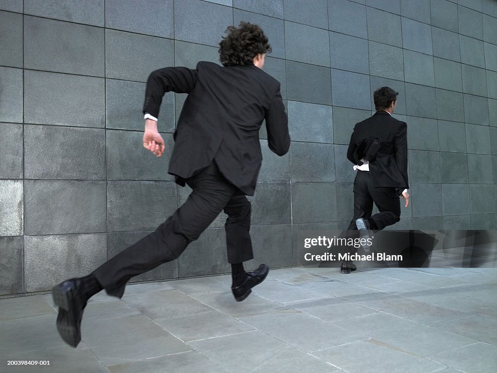 Two businessmen running along street, rear view