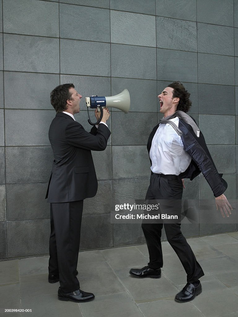 Two businessmen shouting at each other, one using megaphone, side view