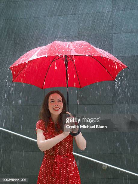young woman standing under umbrella in rain, looking up, close-up - chapéu vermelho imagens e fotografias de stock