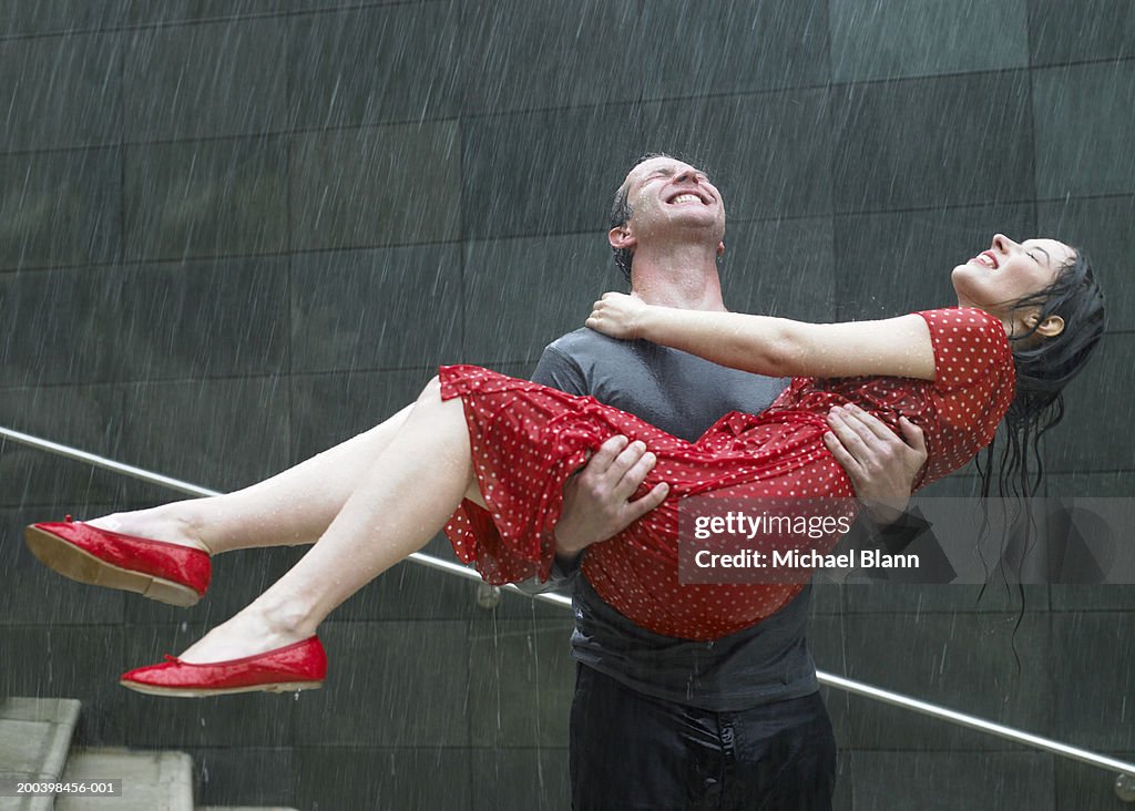 Couple on steps in rain, man carrying young woman, eyes closed