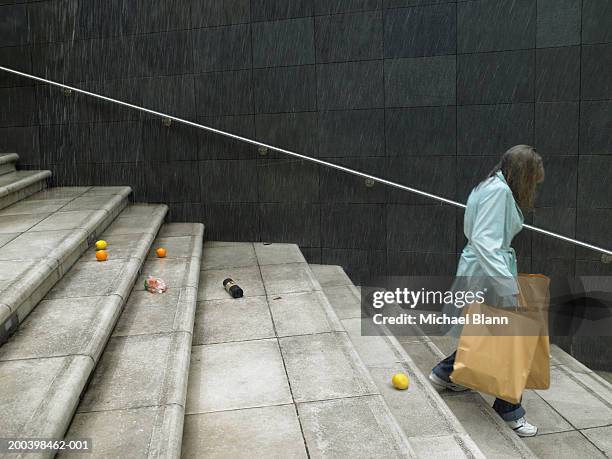mature woman carrying shopping bags down steps in rain, side view - ignorance stock pictures, royalty-free photos & images